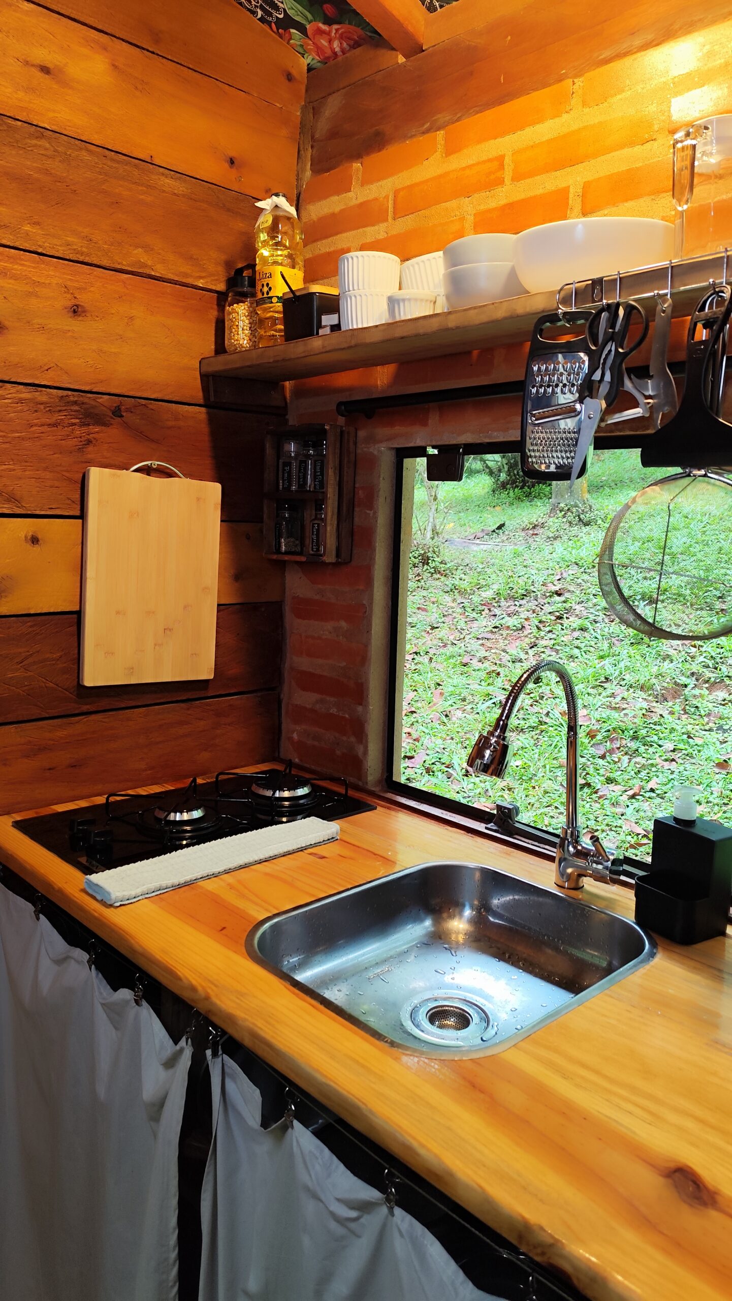 Bancada da cozinha, fogão e pia da cabana organizada com itens essenciais de culinária, unindo funcionalidade e decoração rústica.