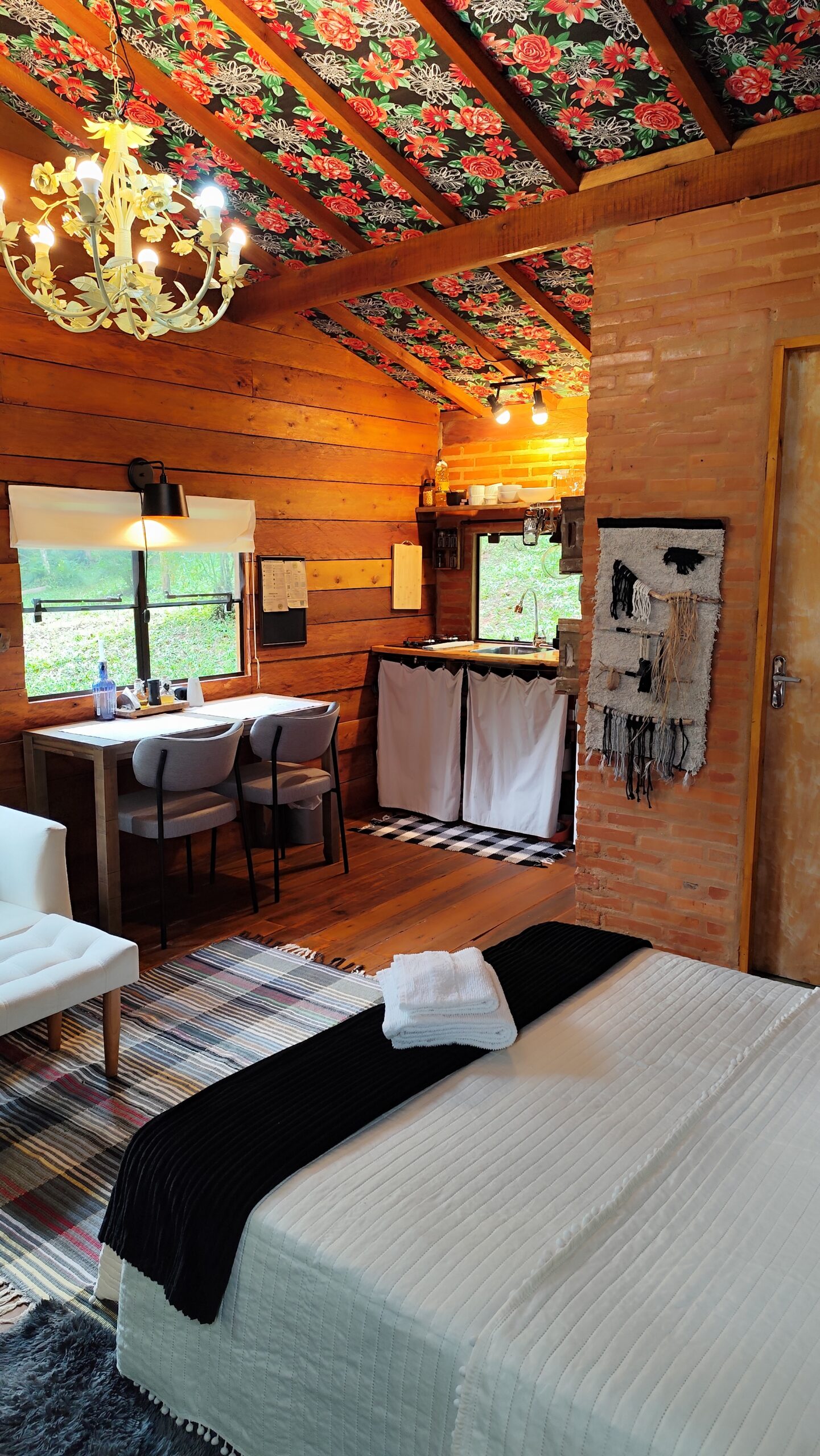 Vista de quarto cozinha ao fundo e lustre de flores e espaço para refeição em cabana lúdica.