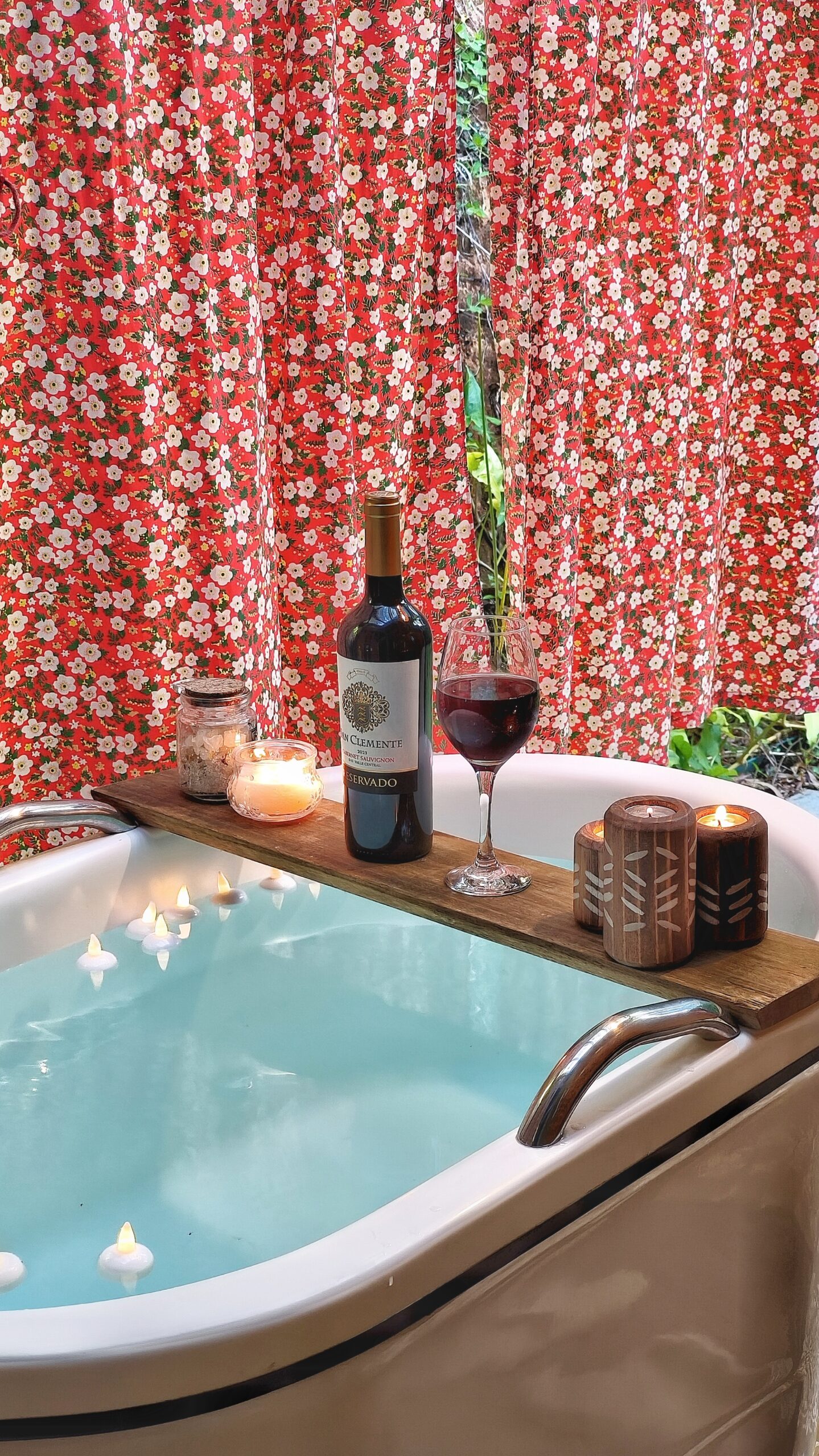 Banheira Ofuro com tábua e em cima taças de vinho, velas e sais de banho que transmite descanso e relaxamento.